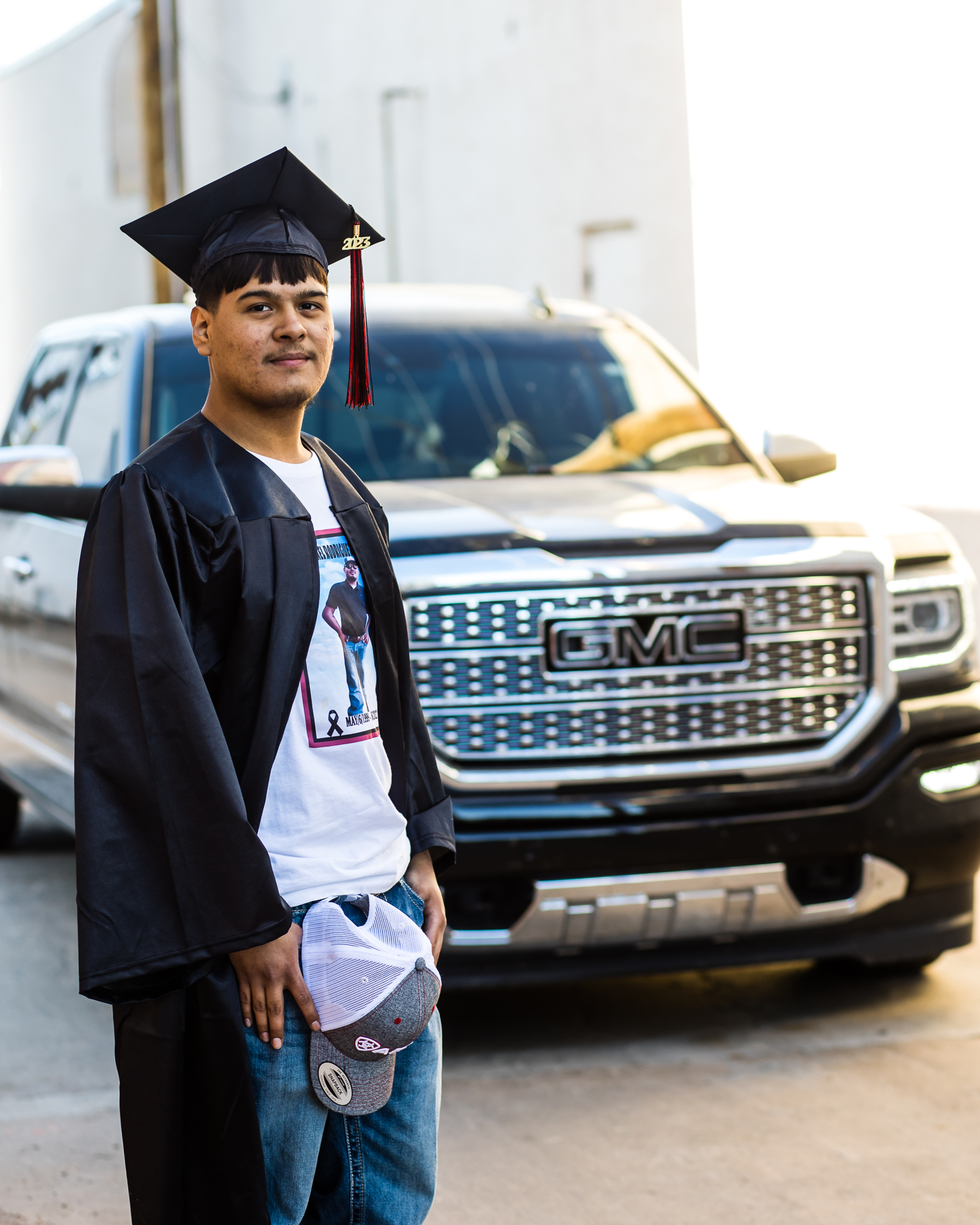 young man in his graduation hat standing in front of his lowered silverado truck