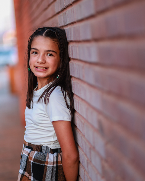 little girl smiling at the camera while laying back on a brick wall